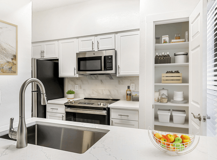 VIrtually staged kitchen with white cabinetry, white quartz countertops, stainless appliances, goose neck faucet and sprayer, pantry, subway tile backsplashj
